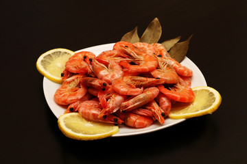 Fresh, delicious, juicy, grilled shrimp with lemon and spices in a white plate on a black table.