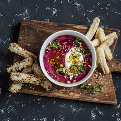 Vegetarian beet hummus and puff pastry bread sticks on a wooden rustic board on a dark background
