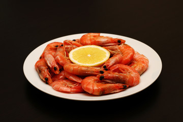 Fresh, delicious, juicy, grilled shrimp with lemon and spices in a white plate on a black table.