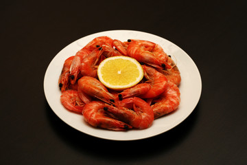 Fresh, delicious, juicy, grilled shrimp with lemon and spices in a white plate on a black table.