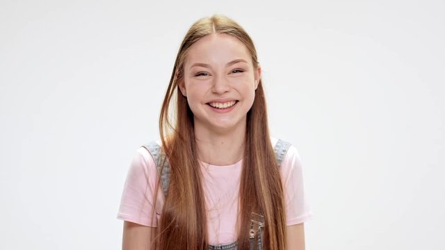 Young beautiful girl showing tongue, laughing over white background. Slow motion.