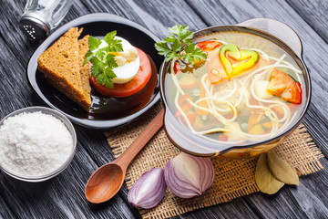 Fresh vegetable soup with noodles in a pot on black