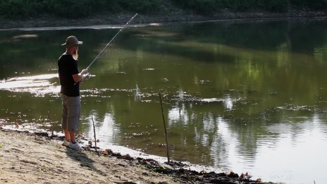 Sports fisherman fishing at lake using spinning rod and wheel, and casting technique