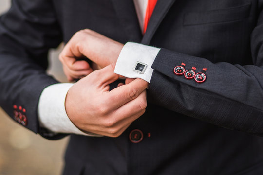 Elegant young fashion man looking at his cufflinks while adjusting them. Color close up image of male hands. Handsome groom dressed in black formal suit, white shirt and tie getting ready for wedding