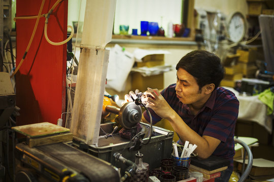 A craftsman at work sitting using a grinding machine to etch and mark a pattern on a glass object.