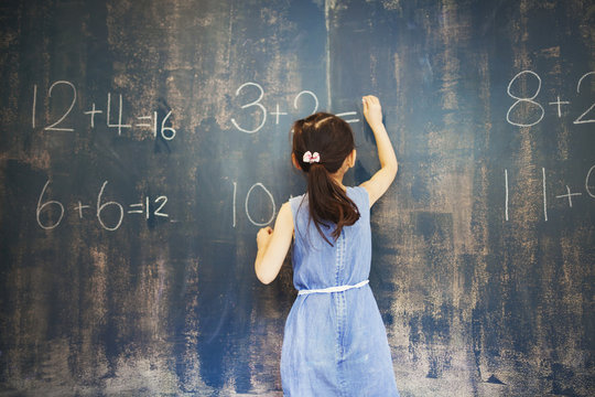 Girl writing with chalk on blackboard