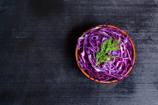 Shredded red cabbage in clay bowl on black background. Vegetarian healthy food. Top view