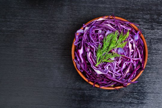 Shredded red cabbage in clay bowl on black background. Vegetarian healthy food. Top view