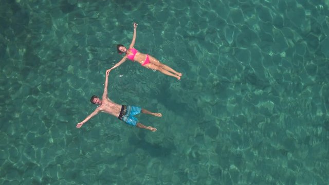 AERIAL: Loving couple on dreamy holidays swimming starfish float holding hands