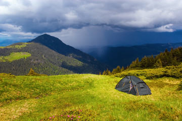 Opposite a high green mountain stands a tourist tent.