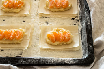 Buns of Fillo Dough with custard and mandarin slices on a baking sprinkle with flour