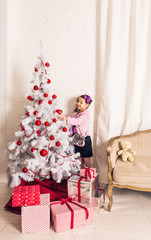 8 years old little girl decorating Christmas tree at home.