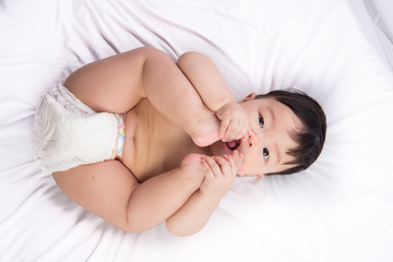 Fototapeta na wymiar Portrait of cute Little asian boy 6 months old put his toe feet in the mouth on the white bed