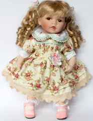 Isolated porcelain blonde haired girl doll in floral dress and pink shoes 