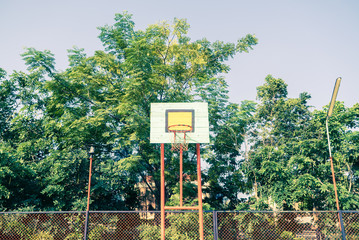 Basketball hoop in the park with green trees in background. Vintage filter style