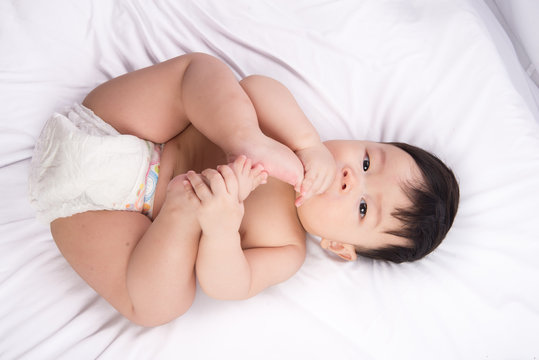 Portrait of cute Little asian boy 6 months old put his toe feet in the mouth on the white bed