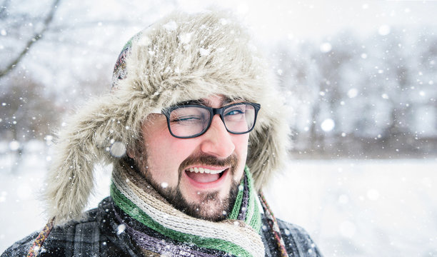 Adult man with beard wearing glasses. The man smiles. Winter, snow, a man in a fur hat. Man winks