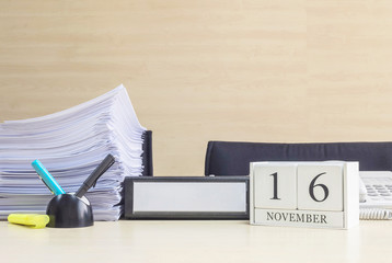 Closeup white wooden calendar with black 16 november word on blurred brown wood desk and wood wall textured background in office room view with copy space , selective focus at the calendar