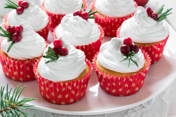 Obraz na płótnie Canvas Christmas cupcakes with vanilla frosting, cranberries and rosemary on white wooden background. Selective focus