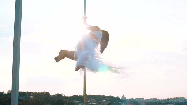 Sexy attractive girl poledancer performs advanced pole dance tricks at sunset on portable dancing stage over the skyline.