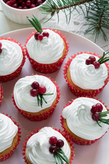 Christmas cupcakes with vanilla frosting, cranberries and rosemary on white wooden background. Selective focus