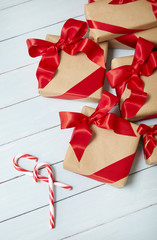 Christmas gifts wrapped in brown paper with red silk bows and candy canes on a painted wooden background