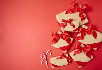 Christmas gifts wrapped in brown paper with silk bows on a bright red background, with candy canes and blank space at side
