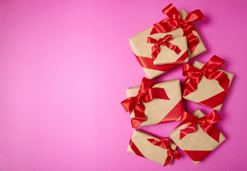 Christmas presents wrapped in brown paper with red silk bows on a bright pink background with blank space at side