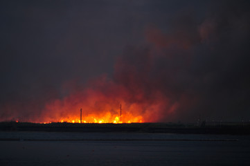 A large fire in a field near the water