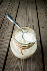 Homemade organic yogurt in a jar with a spoon on a rustic wooden table, copy space