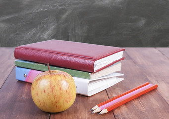 Stack of books, pencils and yellow apple