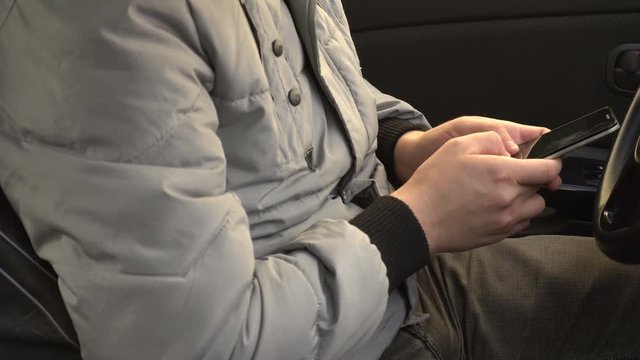 man uses a smartphone while sitting behind the wheel of a car