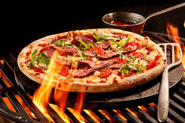 Flames reaching up toward pizza on grill