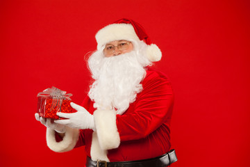 Photo of Santa Claus gloved hand with giftbox, on a red background. Christmas