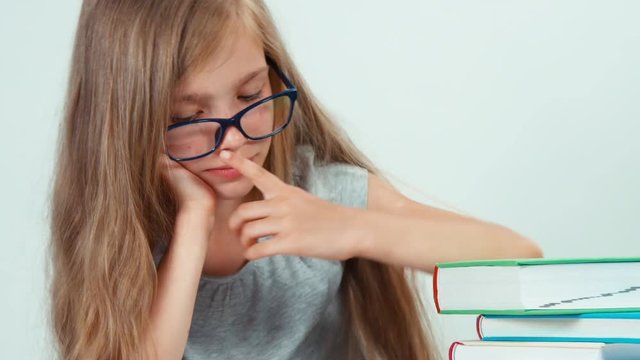Close up portrait student girl with long blond hair 7-8 years in glasses reading book and adjusts glasses. Zooming
