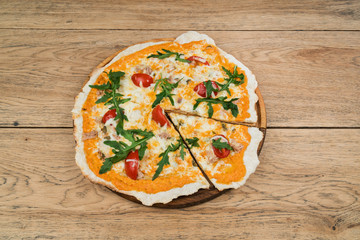 Cheese pizza with cut slice with tomato and fish decorated ruccola and served on a wooden round tray