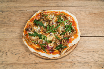 Pork pizza with mushrooms and cheese, decorated with leaves of arugula, served on a wooden tray on old wood table