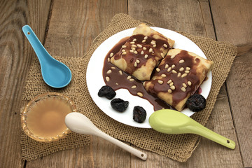 Pancakes with berries, fruits, chocolate, pine nuts and honey on white plate on a natural wooden board