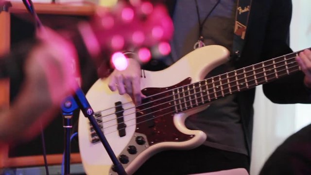 Playing bass guitar rock music close up focus shift to electric guitar fret board with fingers pressing chords. Rock grunge boys band at stage performing at prom or concert gig club enthusiastically