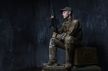 Young soldier sitting on crates of rifle and confidently looks ahead.The soldiers - our pride