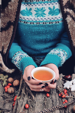 A fall time photo of a female in a blue sweater holding a cup of tea