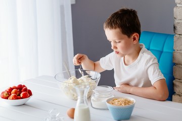 Boy adding sugar to white cheese in bowl for cheesecake.
