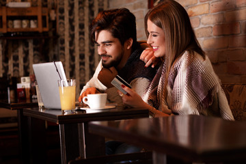 Beautiful young couple with laptop in cafe, they are shopping on line with credit card.
