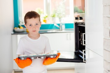 Child holding baking tray with cupcakes