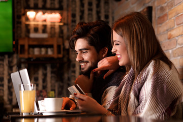Beautiful young couple with laptop in cafe, they are shopping on line with credit card.