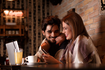 Beautiful young couple with laptop in cafe, they are shopping on line with credit card.