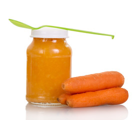 Jar of carrot puree with spoon isolated on white background.
