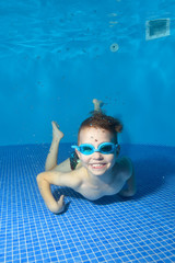 A little boy lies underwater at the bottom of the pool, looks at me and smiles widely. The view...