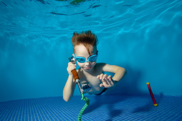 Little boy underwater in swimming pool lies at the bottom and talking on the phone. Shooting under...