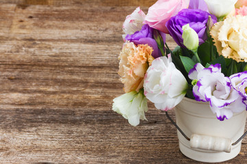 Pink, white and violet eustoma flowers in pot on aged wooden background